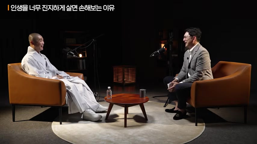 어두운 스튜디오에서 보만 스님과 진행자가 마주 앉아 ‘인생을 너무 진지하게 살면 손해보는 이유’라는 제목 아래 대화하는 장면